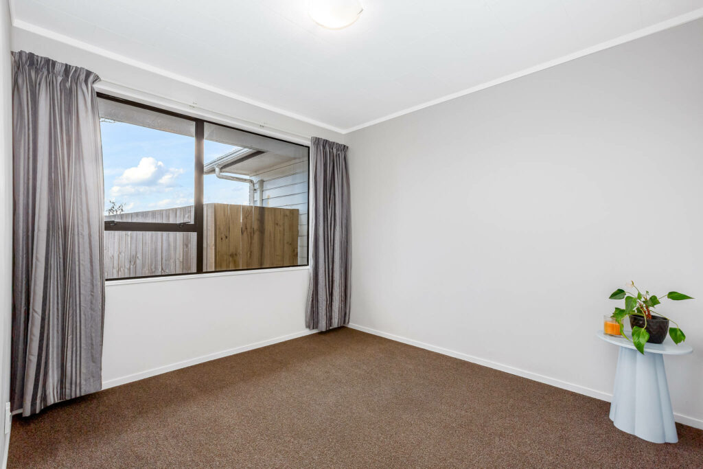 Empty bedroom with gray walls, brown carpet, and a large window.