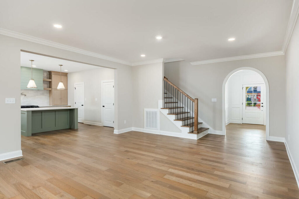 Empty open-concept living area before virtual home staging, featuring the kitchen and staircase.