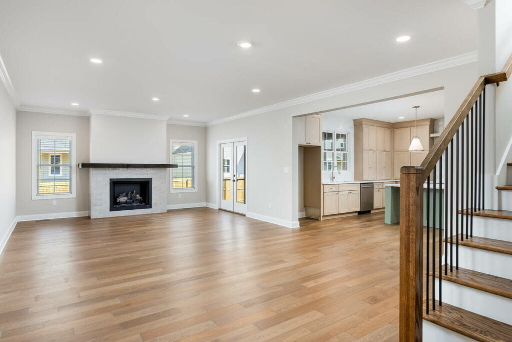 Empty open-concept living room with fireplace, kitchen, and staircase before virtual home staging.