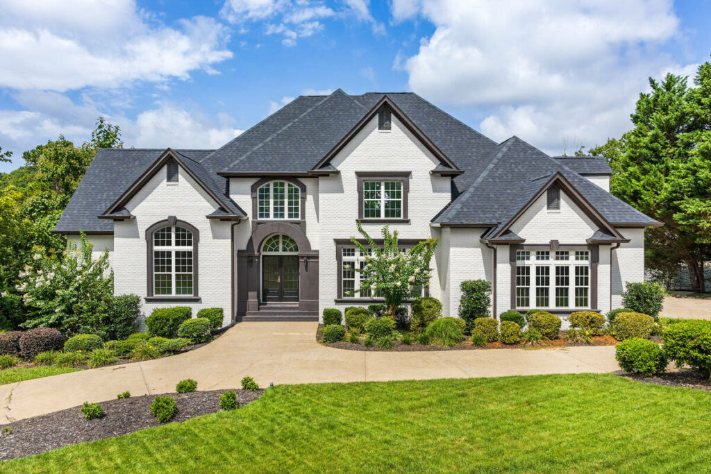 AI real estate photo editing improving a white brick home with vibrant landscaping and crisp architectural details.
