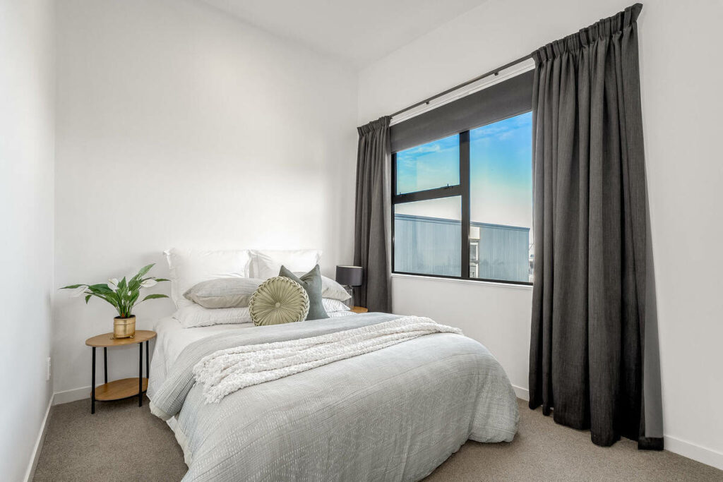 Architecture photography of a bright bedroom with neutral decor and a large window.