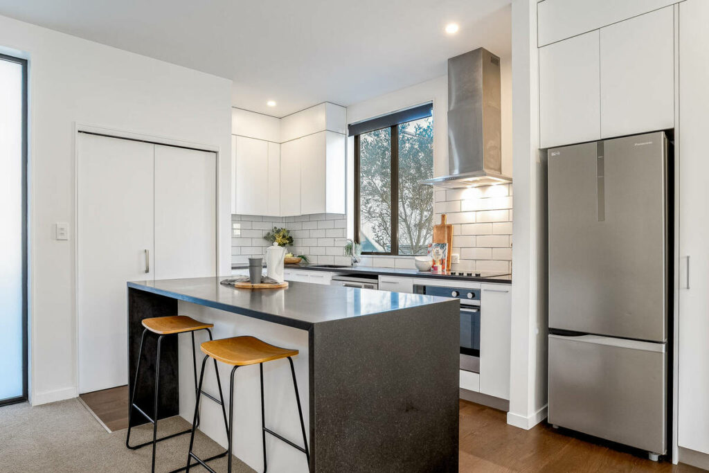Architecture photography of a bright modern kitchen with white cabinetry and a dark island.