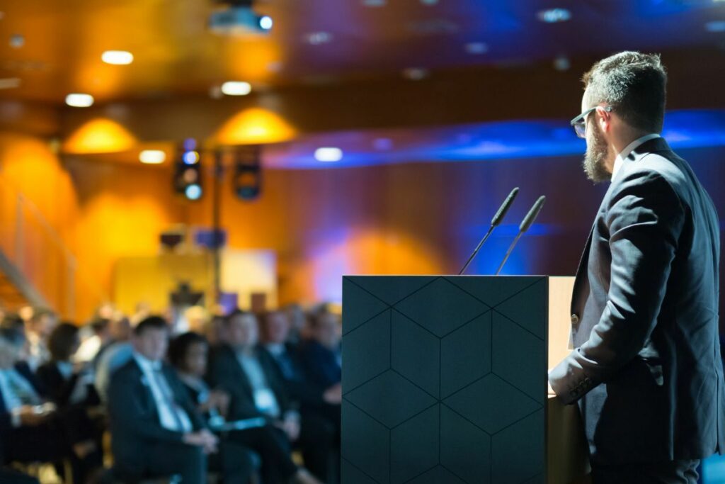 Corporate event photography of a speaker presenting on stage at a conference