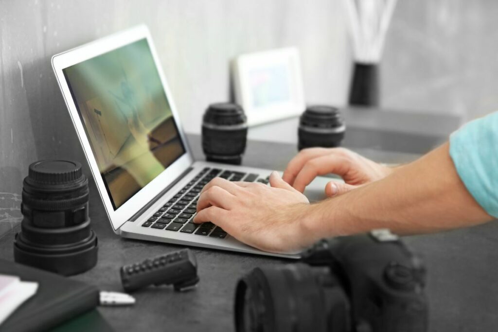 Photographer working on a laptop with cameras and lenses while managing photography business tasks